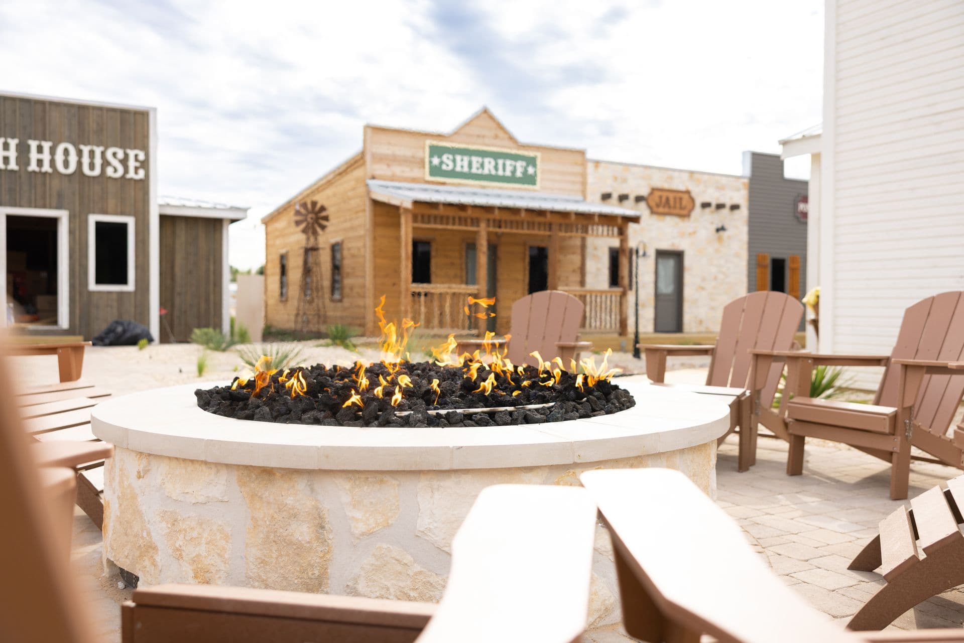 A stone fire pit burning between Adirondack chairs in the western village