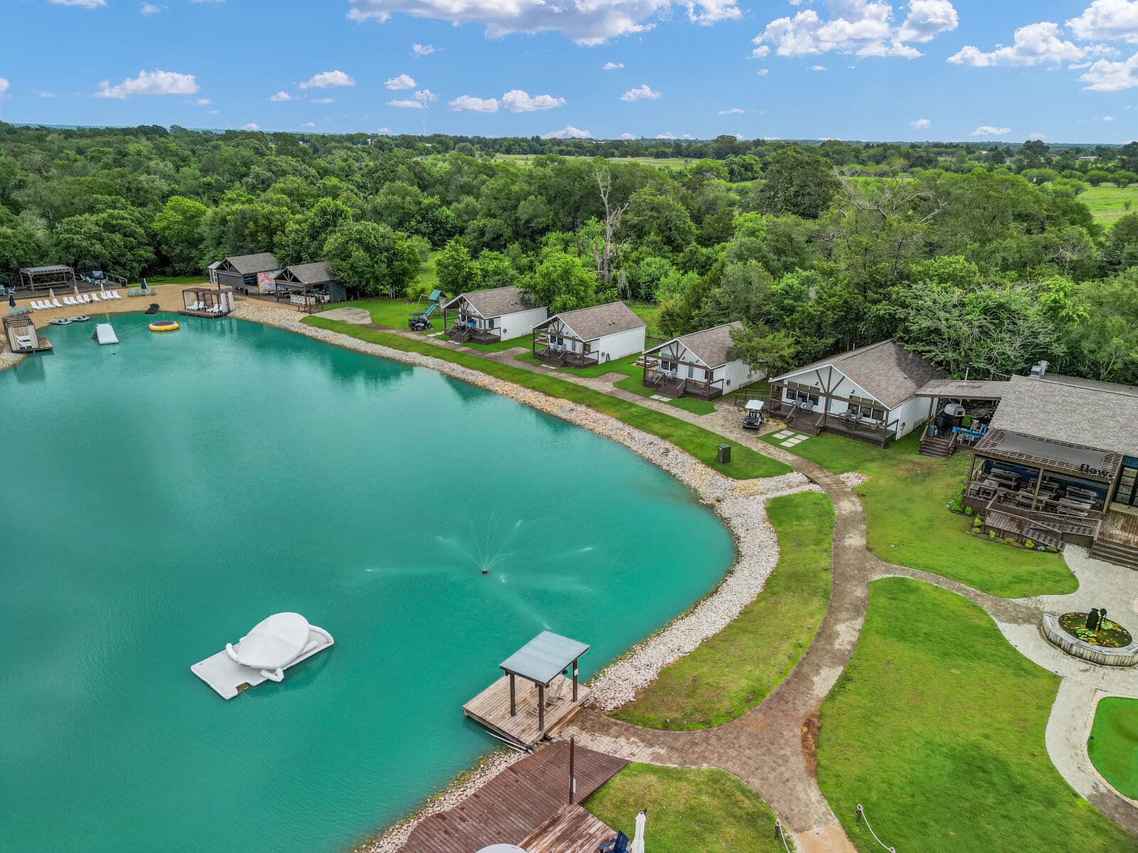 The spring-fed lake from above, turquoise water edged by a sandy beach, a dock, and a row of cabins